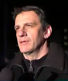 Viktor Jelenic steht mit dunkler Jacke vor dunklem Hintergrund und schaut nach rechts vorn.