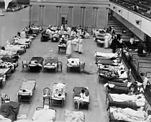 dutzende Betten mit liegenden oder sitzenden Grippeerkrankten in einem Hörsaal in Oakland, betreut von mehreren Krankenschwestern und Ärzten mit Masken