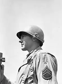 Schwarzweißfoto eines amerikanischen Soldaten während des Zweiten Weltkriegs. Er blickt nach links, sein Oberkörper ist etwa bis zur Hälfte zu sehen. Auf dem Kopf trägt er einen leicht in den Nacken gerutschten Helm, dessen stählerne, kuppelförmige Schale die Ohren halb verdeckt. Der Rand des Helms ist etwas nach außen gezogen, Vorne und hinten etwas stärker, so dass eine Art Schutzschirm entsteht. Die Kinnriemen sind hochgeschlagen und werden durch ein den Helm umlaufendes Band gehalten.