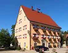 dreigeschossiges Gebäude, mit hohem Satteldach und Wirtshausausleger, rot-weiß-rote Fensterläden