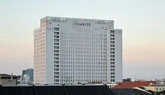 Frontale Farbfotografie eines weißen Hochhauses mit der Aufschrift „Charité“ auf dem Dach.