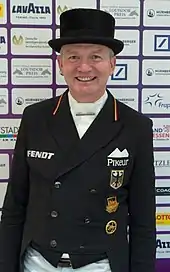 Das Foto zeigt das Gesicht des Dressurreiter Hubertus Schmidt. Er trägt einen schwarzen Zylinder und einen schwarzen Frack.