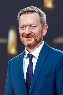 Michael Kessler in dunkelblauem Anzug vor Sponsorenwand