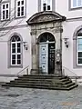 Barockportal der Westfassade des Kollegiengebäudes. Im Tympanon befindet sich zwischen zwei Allegorien ein Wappenschild mit Initialen GA des Universitätsgründers Kurfürst Georg August von Braunschweig Lüneburg (bzw. dem englischen König Georg II.), 2023