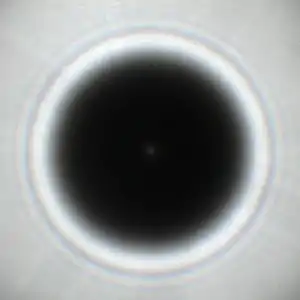 Fotografische Aufnahme des Beugungsmusters mit einem Poisson-Fleck in der Mitte im Schatten eines kreisförmigen Hindernisses mit 5,8 Millimeter Durchmesser in Licht einer ungefähr 0,5 Millimeter großen, ungefähr anderthalb Meter entfernten Lochblende mit Sonnenlicht aus ungefähr 1,8 Metern Entfernung.