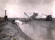 Schwarz-Weißbild eines Eimerbaggers der einen Fluss ausgräbt