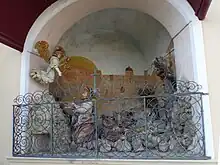 Die im unteren Teil von einem Rankengitter abgeschlossene Nische der Ölberggruppe. Die Jesusfigur blickt zu einem über ihm schwebenden Engel, während Jesus’ Jünger hinter ihm schlafend liegen. Die Rückwand der Nische ist mit der Darstellung eines großen, sandfarbenen Gebäudes bemalt.