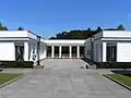 Gebäude hinter dem Ehrenmal. Dokumentation zum Zweiten Weltkrieg und Zugang zu den Grasflächen.