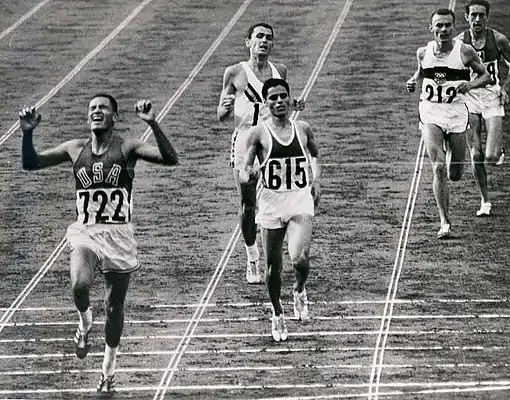 Zieleinlauf im 10.000-Meter-Finale 1964: Mit der 722 der Olympiasieger Billy Mills aus den USA, mit der 615 Mohammed Gammoudi aus Tunesien mit Silber. Direkt hinter Gammoudi Ron Clarke auf Platz 3