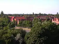 Blick von Elmschenhagen-Süd nach E.-Nord über den „Elmschenhagener Kreisel“: hinter den Bäumen die „Preetzer Chaussee“ (B76), nach links Richtung Kiel, nach rechts Richtung Preetz; am Horizont der Tele-Aufnahme sind das Y-Wohn-Hochhaus sowie links davon der Wasserturm des Kieler Ostufer-Stadtteiles Dietrichsdorf zu erkennen (Aufnahme Juni 2008).