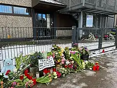 Blumen vor dem Eingang, darauf ein Schild mit der Aufschrift „Trauer – und Wut über das fehlende Waffenverbot“