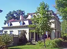 Ein Haus mit gekurvtem Dach und einem kleinen Baum im Vordergrund (Sicht von der Seite)