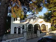 Kircheneingang der Kirche Agios Chrysostomos, Chaniotis. Dreibogiger Eingang unter einer großen Kiefer.