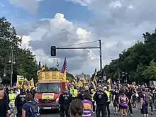 Demonstrationszug mit Lautsprecherwagen (links), Teilnehmenden (rechts), Fahnen und Transparenten.