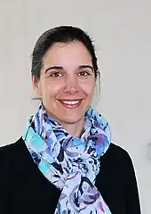 Eine Frau mit schwarzem Pullover, dunklen nach hinten gebundenen Haaren und einem großen Tuch in blauen Farben um den Hals