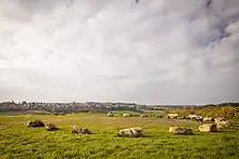 Foto einer Hügelkuppe mit in einem Kreis angeordneten Steinen und drei Bänken. Im Hintergrund sieht man städtische Bebauung.