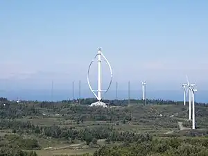 Der Darrieusrotor Éole. Seine Größe wird im
Vergleich mit den Bäumen und den anderen Windrädern ersichtlich.