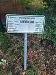 Schild für Merkur in unmittelbarer Nähe der Sonne, rund 58 Meter entfernt in Rufweite, auf der anderen Straßenseite. Vor dem Auge hat die Sonne knapp den dreifachen Durchmesser und die neunfache Fläche als die echte Sonne von der Erde.