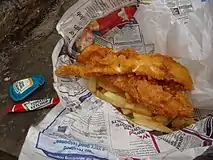 Fish ’n’ Chips mit Papierschutz vor der Druckerschwärze der Zeitung und Soßenbeutel