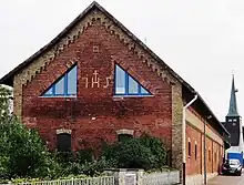 IHS als Klinker-Ornament in der Giebelmauer eines Wirtschaftsgebäudes