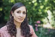Porträtaufnahme von Gilda Sahebi; das Motiv steht in der linken Bildhälfte und schaut zur betrachtenden Person, die rechte Bildhälfte zeigt den Hintergrund mit Natur