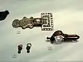 Aus einem Mädchengrab (Grab 438): Bronzefibel, gegossene silberne Bügelfibel (Typ Nocera Umbra), kreisaugenpunzierte, pyramidenförmiger Ohrringe; Ende 6./Anfang 7.&nbsp;Jahrhundert.