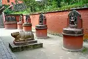 Statuen des Nandi (im Vordergrund), des Pande und seiner zwei Frauen, des Vishnu, des bärtigen Brahma, des Brindi Bhairab und des Nandi Bhairab (entlang der Mauer von links nach rechts)