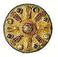 Eine goldene Scheibenfibel mit aufwendiger Verzierung in Gold und Edelsteinen.