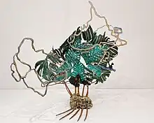 Bronzeskulptur mit üppigen grünen Blättern einer Monstera-Pflanze und mäandrierenden kartografischen Linien, sowie perforierte blauen Abstraktionen aus Karten des Meeresbodens.