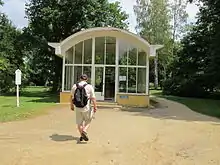 Mann mit Rucksack geht auf einen Glaspavillon mit Tonnendach zu