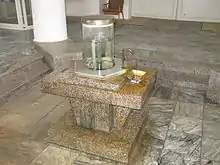 Steinsockel mit Wasserhahn und mit Wasser gefüllter Glassäule