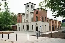 Eine Fassade mit zwei kleineren, seitlichen und einem größeren Turm in der Mitte. Davor ein geschotterter Platz.