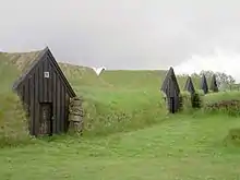 Eine Reihe niedriger Häuser mit dunkler Holzfront und grasbewachsenen Dächern