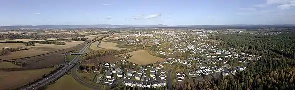 Foto einer von Wald und Feldern umgebenen Stadt in flacher Landschaft  mit einer breiteren Straße links im Bild