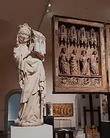 Eine Kalkstein Figur, die Königin Johanna I. von Navarra, Frankreich, mit einem Kapellenmodell in den Händen zeigt. Ausstellungsansicht im Berliner Bode-Museum
