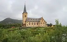 Foto einer Holzkirche, im Hintergrund eine Erhebung