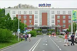 Ein Hotel mitten in einem Gewerbegebiet (Aufnahme mit Teleobjektiv aus weiter Entfernung).Bereits bei diesem Bildausschnitt sind viele Details der Umgebung nicht mehr zu sehen: Baumärkte, Möbelhaus, Hochspannungsleitungen, Trubel und viel Verkehr.
