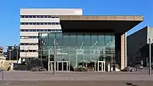 Blick auf das Eingangsgebäude der TU Darmstadt vom Karolinenplatz aus. Im Hintergrund sind das Audimax, das Karl-Plagge-Haus, das Verwaltungsgebäude und das Kongresszentrum Darmstadtium sichtbar,