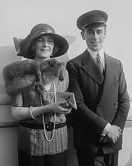 Edwina und Louis Mountbatten sind nebeneinander stehend fotografiert. Die Fotografie ist in schwarz-weiß. Edwina M. trägt einen großen Hut und trägt einen Pelzschal. Sie hält eine kleine Tasche. Louis M. trägt einen Hut und einen Anzug.