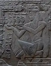 Relief eines kunstvoll gekleideten Mannes, der kniend ein Tablett mit Speisen und Blumen hält