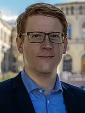 Foto eines Manns mit Brille, im Hintergrund ist das norwegische Parlamentsgebäude zu erkennen
