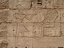 Relief eines Mannes mit Krone, der ein Tablett mit Speisen vor einem sitzenden Mann mit Widderkopf hält