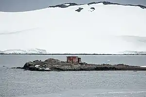 Die kleine Insel D’Hainaut im Mikkelsen Harbor, mit der argentinischen Schutzhütte und zahlreichen Eselspinguinen, und im Hintergrund die vergletscherte Steilküste der Trinity-Insel