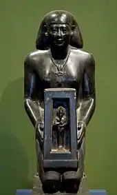 Statue eines knienden Mannes, der ein Kästchen mit einer kleinen männlichen Figur hält