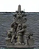 52. Trophäe –  Fiale, 2 Putten, Löwenkopf, Löwenpranke, Peltaschild mit Gorgonenhaupt, Goldenes Vlies, Kugeln.