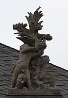 54. Trophäe –  Baumstamm, Löwe, Widder, Putto als Kronenhalter.