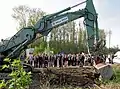 Der vom Innenminister Joachim Herrmann bediente Kettenbagger Liebherr R 944 mit Verstellausleger, im Hintergrund Zuschauer und protestierende Umweltaktivisten