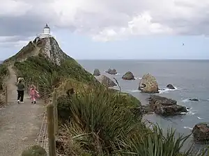 Blick entlang des Zugangswegs Richtung Nugget Point Lighthouse. Im Hintergrund sind die dem Kap namensgebenden Felsen zu sehen („The Nuggets“).