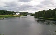 Foto eines breiteren Flusses in bewaldeter Landschaft, am Ufer links im Bild vereinzelte Häuser