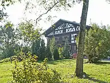 zweigeschossiger, teils verbretterter Blockbau mit Flachsatteldach, Fachwerkteil und -giebel